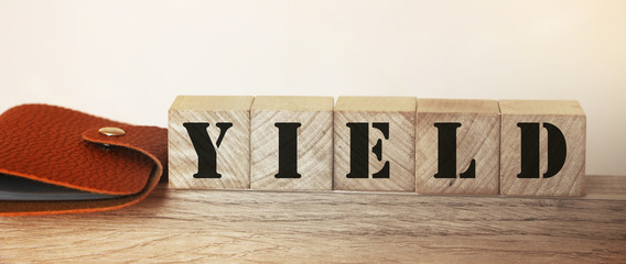 Yield Word on Wooden Cubes and brown leather wallet on wooden table. Harvest profit business concept