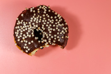 Bitten tasty chocolate donut on a pink background. Top view