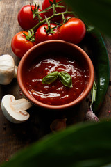 selective focus of delicious tomato sauce in bowl near mushrooms, tomatoes and spices on wooden board