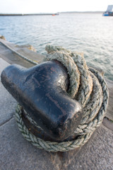 close-up of a quayside mooring bollard with thick rope tied around it