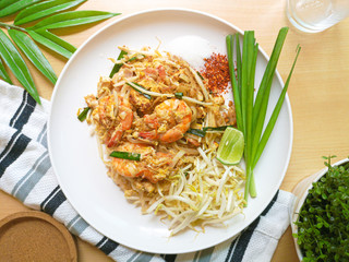 Top view of Thailand traditional style noodles food , stir-fried rice noodles with Shrimp call Pad Thai Goong Sod on white plate with chili sugar peanut and lime for seasoning on wooden table.