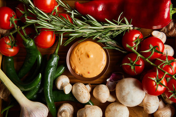 top view of delicious sauce in bowl near fresh ripe vegetables, rosemary and mushrooms