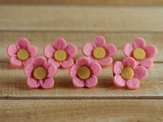 Obraz na płótnie Canvas 7 pink felt flowers with yellow centers lined up on a piece of real wood. Perfect for crafts or accessories.