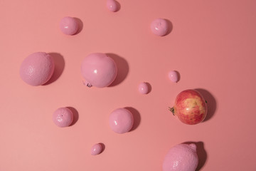 Pink fruits and one natural pomegranate on pink background. Artificial fruits demonstration. Conceptual top view photo. Be yourself concept. Copy space