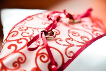 Wedding rings laid on a satin cushion decorated with a red decorated ribbon