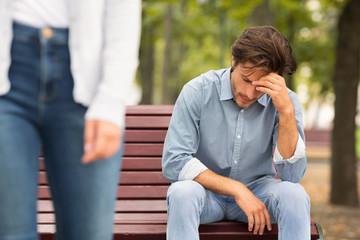 Unrecognizable Girlfriend Leaving Sad Boyfriend Sitting On Bench In Park