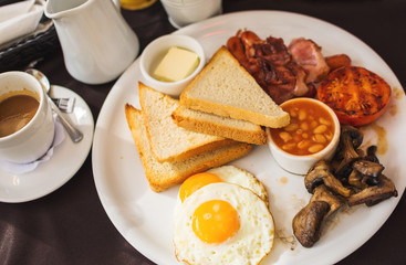 Traditional full English breakfast with fried eggs, bacon, sausages, beans in tomato sauce, toast, fried tomatoes and mushrooms