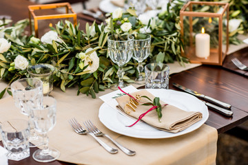 in backyard of villa in Tuscany there is banquet wooden table decorated with cotton and eucalyptus compositions, glasses, candles and plates are placed on table
