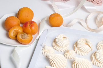 Marshmallows laid out on a tray. Nearby are ripe apricots.