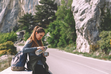 Naklejka na ściany i meble Traveling woman sitting near mountain and looking far away Spring weather, calm scene. Hiking outdoors, landscape view in the sunlight. A series of photos of Wanderlust.