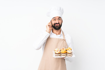 Young man holding muffin cake over isolated white background frustrated and covering ears