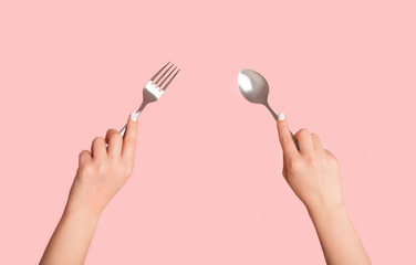 Closeup of female hands holding metal spoon and fork against pink background, panorama