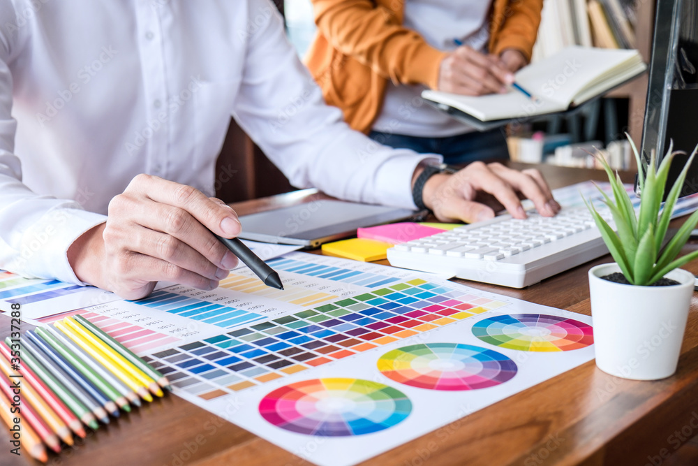 Poster Two colleague creative graphic designer working on color selection and color swatches, drawing on graphics tablet at workplace with work tools and accessories
