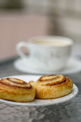 Outdoor breakfast. Freshly baked cinnamon buns and cup of coffee on a glass table. 