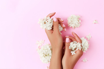 Tender hands with perfect blue and pink manicure on trendy pastel pink background with flowers. Place for text