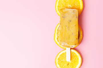 orange ice cream on a stick on a background of slices of orange on a pink background. Hot summer concept. Top view, flat lay.