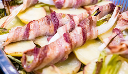 Raw spring onion with rolled bacon. Typical Sicilian street dish called 'Cipollata' roasted on the grill and roasted potatoes as a side dish.
