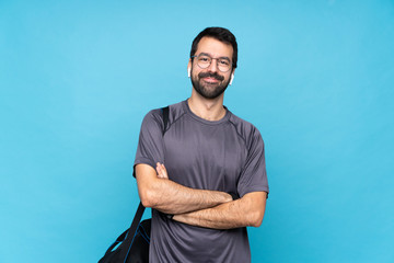 Young sport man with beard over isolated blue background with glasses and happy