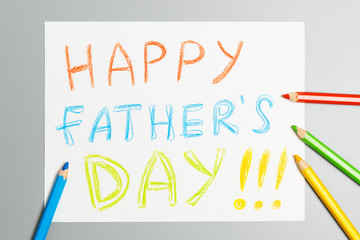  bright inscription "happy father's day" on a white sheet and color pencils on a gray background.