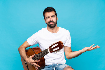 Young man with guitar over isolated blue background unhappy for not understand something