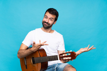 Obraz premium Young man with guitar over isolated blue background extending hands to the side for inviting to come
