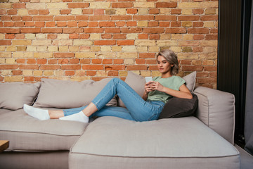 beautiful young woman resting on sofa and chatting on smartphone