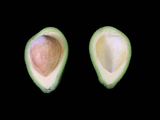 Two halves of avocado with bone, on a black background. Green, ripe avocado vegetable in a cut....