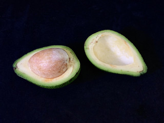 Two halves of avocado with bone, on a black background. Green, ripe avocado vegetable in a cut....