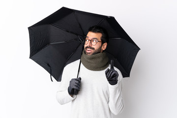 Caucasian handsome man with beard holding an umbrella over isolated white wall thinking an idea pointing the finger up