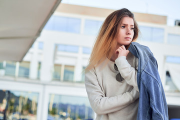beautiful charismatic girl in a light sweatshirt v denim jacket with long blonde hair on a summer day