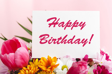 Happy birthday text on card in flower bouquet on pink background. Greeting card in Tulips, daisies, chrysanthemum beautiful spring bouquet. Flower delivery, congratulation card.