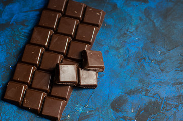 bar of dark chocolate on a blue background with sprinkled cocoa