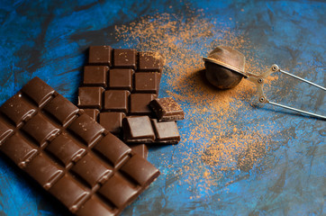 bar of dark chocolate on a blue background with sprinkled cocoa