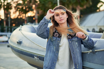 golden backlight, a beautiful girl in sunglasses and a denim jacket with long blonde hair in summer sunset on the background of an inflatable boat in the port