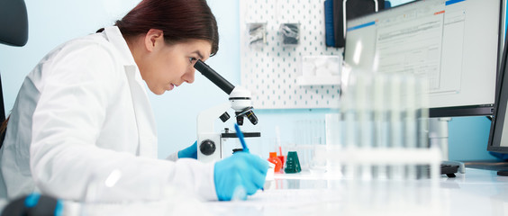 Side view of brunette lab technician looks at microscope in laboratory.