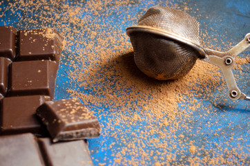 bar of dark chocolate on a blue background with sprinkled cocoa