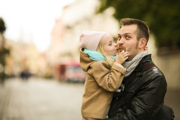 Little girl in beige coat kissing her father in black jacket. Dad hugging his little daughter on the street. Family spending time together in the city. Father's day.