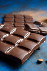 bar of dark chocolate on a blue background with sprinkled cocoa