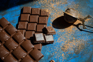 bar of dark chocolate on a blue background with sprinkled cocoa