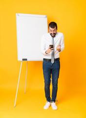 Full-length shot of businessman giving a presentation on white board over isolated yellow background surprised and sending a message