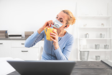 Online teacher with a protective mask tutoring over the internet. Trouble with drinking morning coffee.