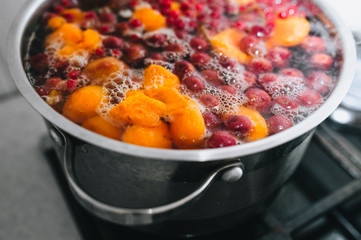 Cooking a delicious compote of apricot, apples, cherries, raspberries. Fresh fruits are boiled in boiling water in a metal pan on the stove. Photography, concept.