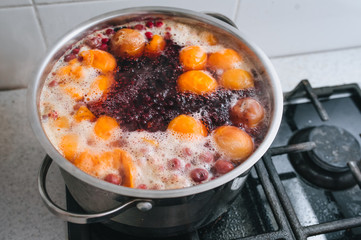 Cooking a delicious compote of apricot, apples, cherries, raspberries. Fresh fruits are boiled in boiling water in a metal pan on the stove. Photography, concept.