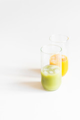 Two glasses with green and orange detox juices and ice cubes on light background. 