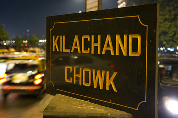 A road sign on Mumbai's Marine drive at Kilachand Chowk clicked at night with vehicles passing behind the road sign. The Kilachand square is a landmark and popular meeting spot for the visitors.