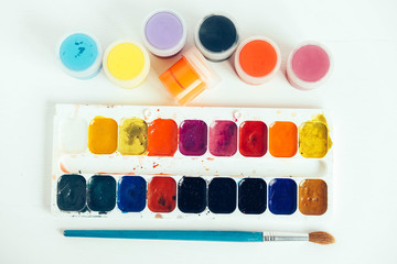 Colorful gouache paints and brush for painting on white wooden table. Top view. Copy, empty space...