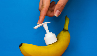 Banana with white dispenser for cosmetics, soap and other hygiene products on blue background. Useful exotic fruit.