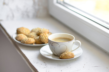 Cup of black coffee and plate with peanut butter cookies on a white table.
