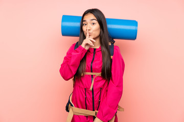 Young mountaineer Indian girl with a big backpack isolated on pink background doing silence gesture