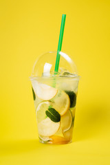 Lemonade to go cup with mint, lime and lemon on bright yellow background, isolated